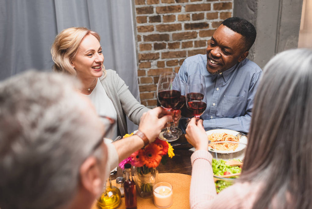 rajattu näkymä naisen ja miehen clinking kanssa hymyilevä monikulttuurinen ystäviä illallisen aikana
  - Valokuva, kuva