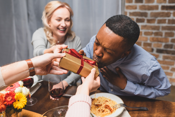 cropped view of man giving present to african american man during dinner  - Foto, Bild