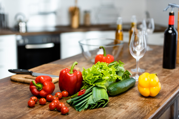 vegetables. bottles with wine and beer, wine glasses, bowl, chopping board, knife on wooden table in kitchen  - Foto, Imagem