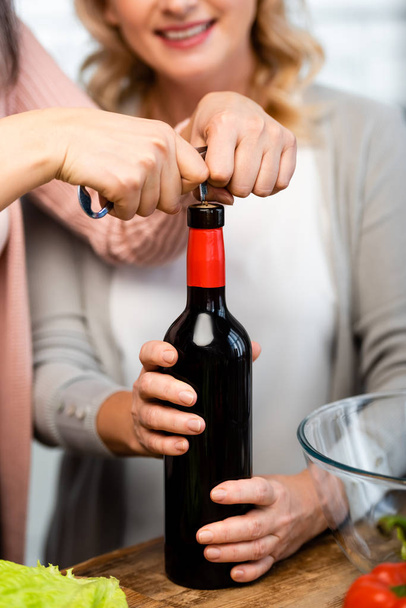 cropped view of friends opening wine bottle with corkscrew in kitchen  - Foto, afbeelding