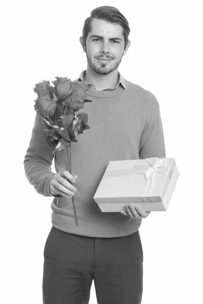junger gutaussehender kaukasischer Mann hält rote Rosen und Geschenkbox für den Valentinstag bereit - Foto, Bild