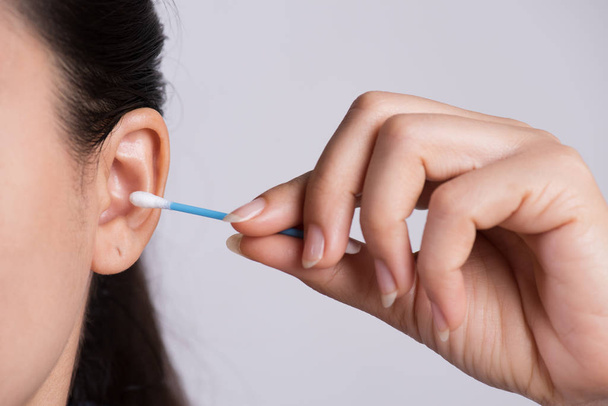 Закройте молодую азиатку, чистящую уши ватным тампоном. Здоровье
 - Фото, изображение