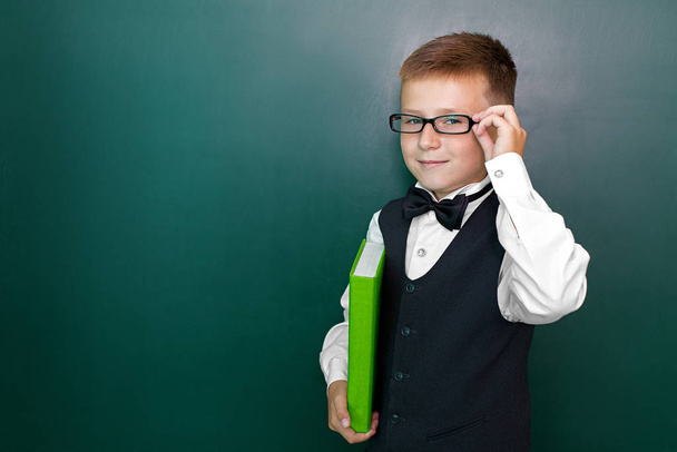 Χαρούμενο χαριτωμένο έξυπνο αγόρι με παπιγιόν και γυαλιά με βιβλίο στο χέρι. Πρώτη φορά στο σχολείο. Πίσω στο σχολείο.. - Φωτογραφία, εικόνα