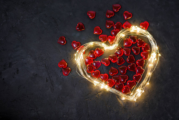 Valentine's day - heart of a garland with lights and red hearts inside on a dark background, place for text, postcard for the holiday - Fotografie, Obrázek