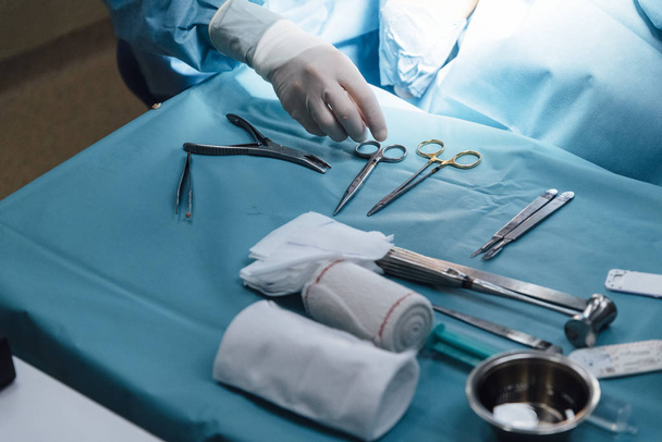 Pohled na sadu lékařských nástrojů umístěných na stole na místě světla v blízkosti nepoznatelného chirurga na operačním sále - Fotografie, Obrázek