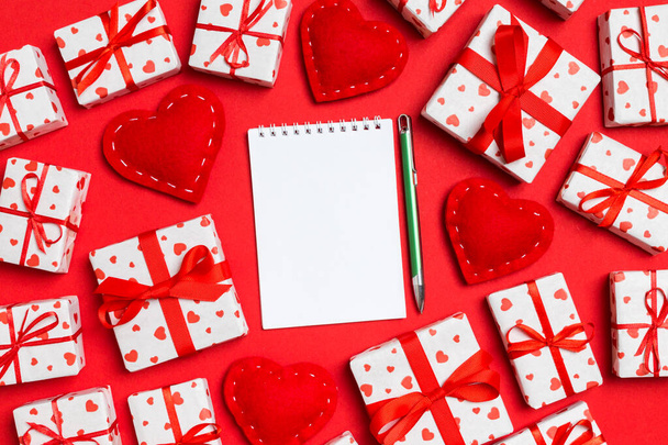 Top view of notebook, white gift boxes and red textile hearts on colorful background. Valentine's Day concept - Photo, Image
