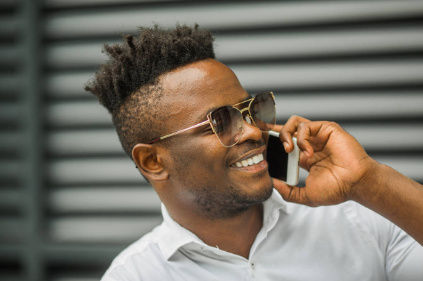 handsome young african man in a white shirt with a phone in his hand - Foto, Imagem