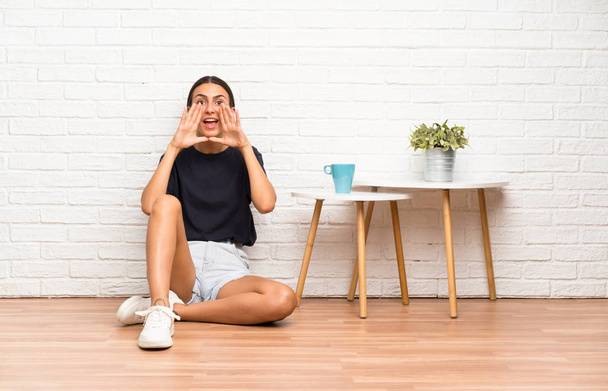 Young woman sitting on the floor shouting with mouth wide open - Photo, Image