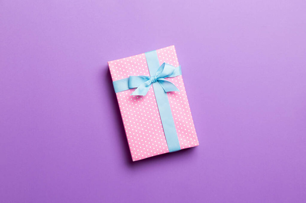 envuelto Navidad u otro regalo hecho a mano de vacaciones en papel con cinta azul sobre fondo púrpura. Caja de regalo, decoración de regalo en mesa de colores, vista superior con espacio para copiar - Foto, imagen