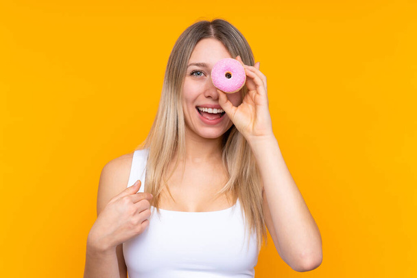 Young blonde woman over isolated blue background holding a donut and happy - 写真・画像
