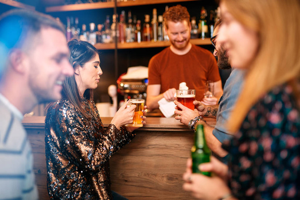 Küçük bir grup insan barda dikilip sohbet ediyor, bira içiyor ve cuma akşamının tadını çıkarıyor. Gece dışarı. - Fotoğraf, Görsel