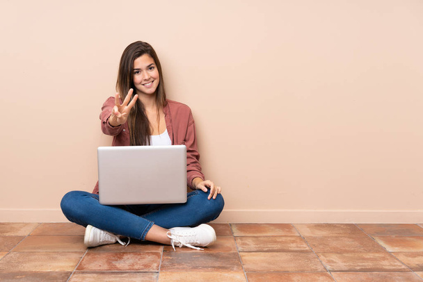 nastolatka student dziewczyna siedzi na podłodze z a laptop szczęśliwy i liczyć trzy z palce - Zdjęcie, obraz