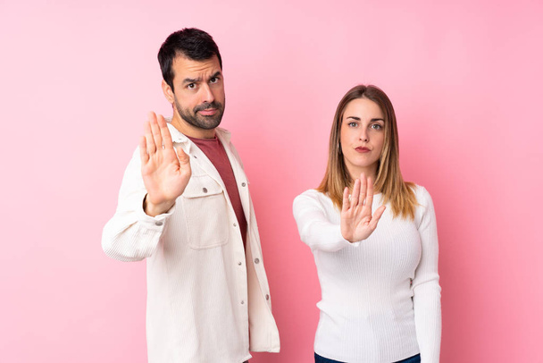Paar in Valentijnsdag over geïsoleerde roze achtergrond maken stoppen met gebaar ontkennen van een situatie die verkeerd denkt - Foto, afbeelding