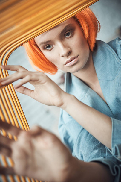 portrait of a beautiful girl with nude makeup and orange short hair holding orange  metal chair by her fingers - Foto, Imagem