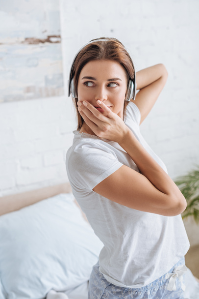 νεαρή γυναίκα που καλύπτει το στόμα και ακούει μουσική στο σπίτι  - Φωτογραφία, εικόνα