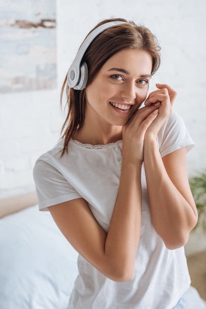 Lächelnde Frau blickt in die Kamera, während sie zu Hause Musik hört  - Foto, Bild