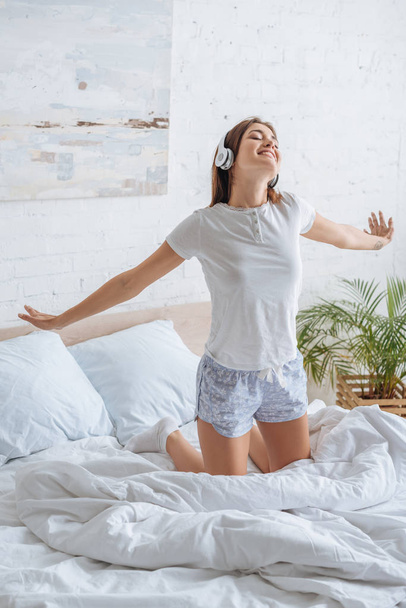 positive girl with outstretched hands listening music in bedroom  - Fotó, kép