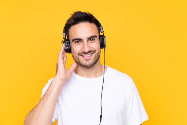 Young man over yellow background listening music - Фото, изображение