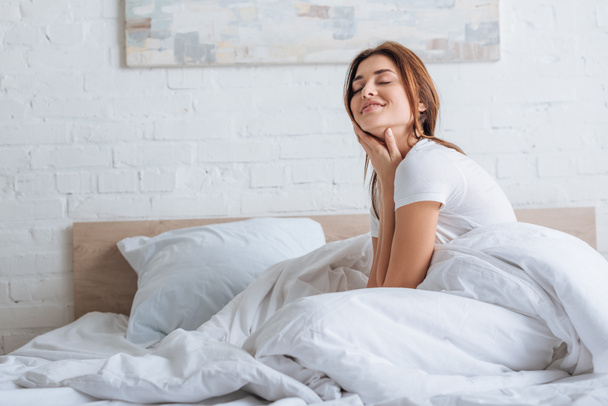 verträumte junge Frau berührt Hals und ruht sich im Bett aus  - Foto, Bild