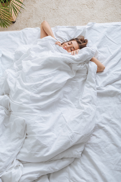 bovenaanzicht van gelukkig jong vrouw bedekt met deken rusten in bed  - Foto, afbeelding