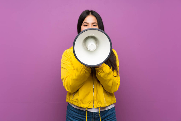 Young teenager Asian girl over isolated purple background shouting through a megaphone - Foto, imagen