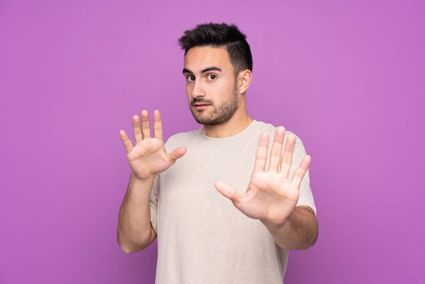 Молодий красивий чоловік над ізольованим фіолетовим тлом нервово розтягує руки на передній план
 - Фото, зображення