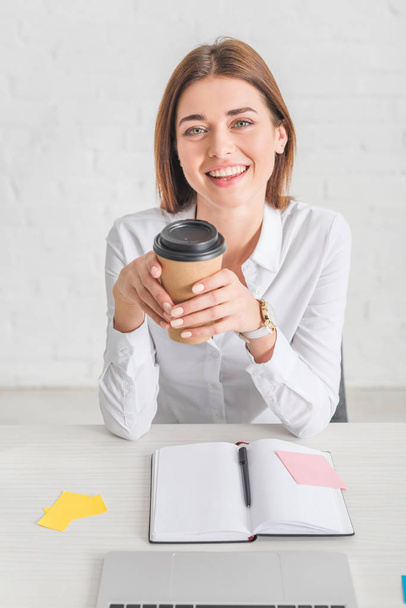 szczęśliwy businesswoman patrząc w aparat i trzymając papierową filiżankę  - Zdjęcie, obraz