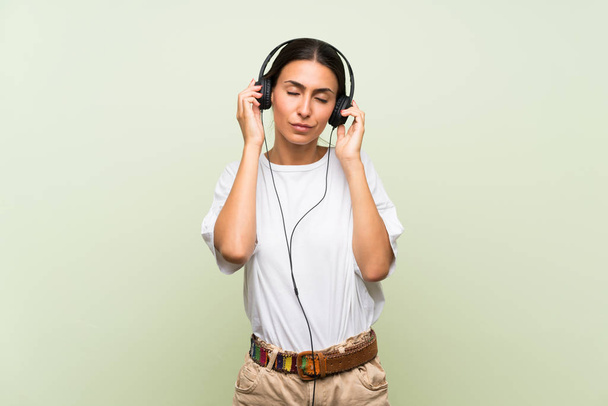 Young woman over isolated green background listening to music with headphones - Foto, immagini