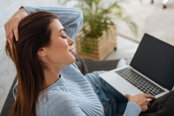 attractive girl with closed eyes holding laptop with blank screen at home  - Photo, Image