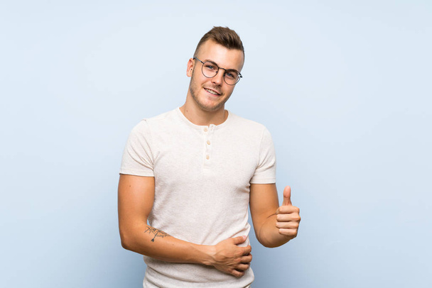 Mladý pohledný blonďatý muž přes izolované modré pozadí s brýlemi - Fotografie, Obrázek