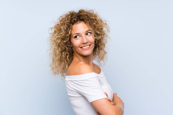 Young blonde woman with curly hair over isolated blue background laughing - Fotografie, Obrázek