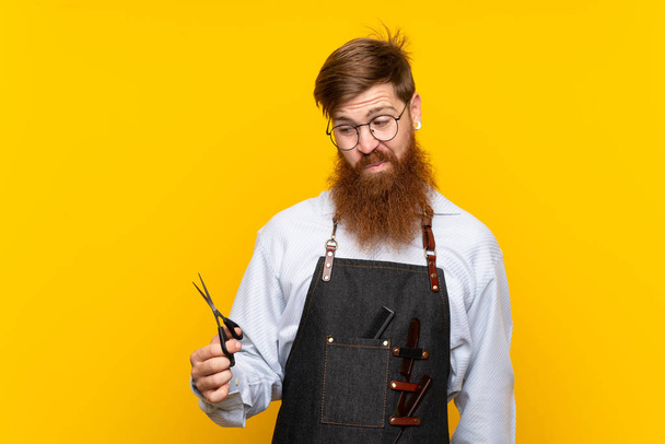 Friseur mit langem Bart in Schürze über gelbem Hintergrund mit traurigem Gesichtsausdruck - Foto, Bild