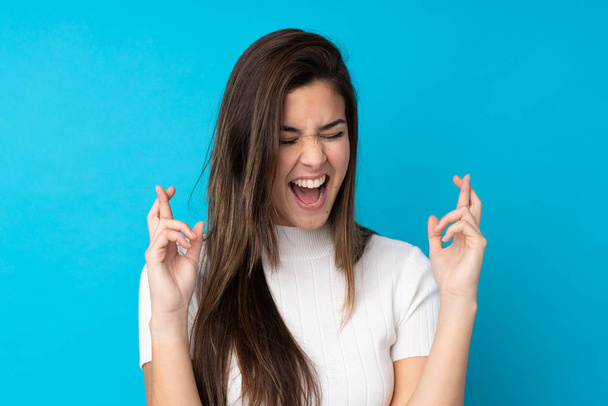 Teenager girl over isolated blue background with fingers crossing - Fotó, kép