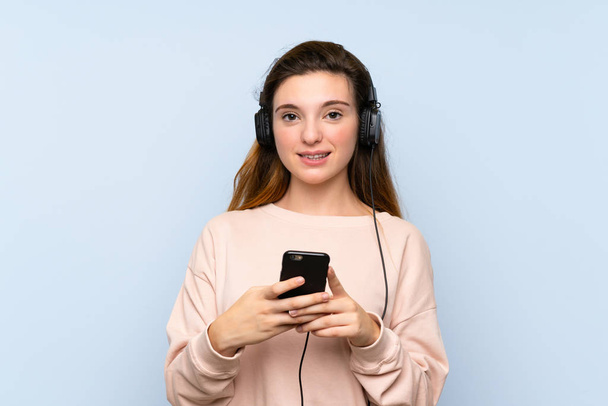 Jeune fille brune sur fond bleu isolé en utilisant le mobile avec écouteurs
 - Photo, image