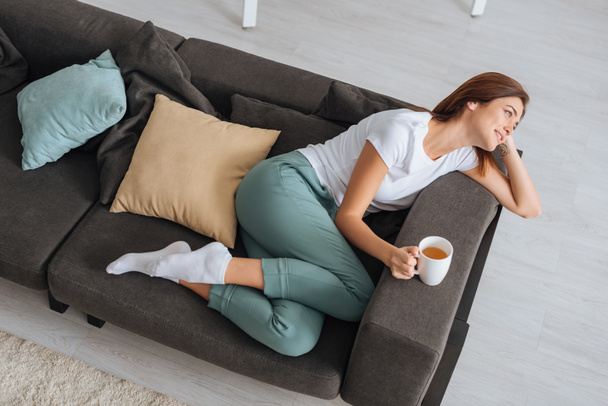 overhead view of attractive woman chilling of sofa with cup of tea  - Фото, изображение