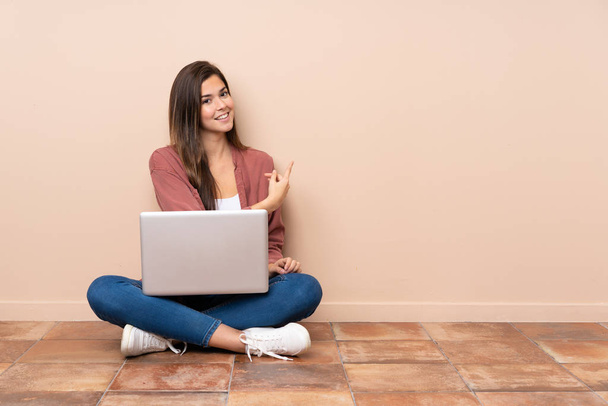 Nastoletnia studentka siedzi na podłodze z laptopem skierowanym do tyłu - Zdjęcie, obraz