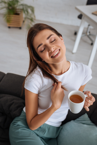 Nuori nainen tilalla kuppi teetä, kun jäähdytys sohvalla olohuoneessa
  - Valokuva, kuva