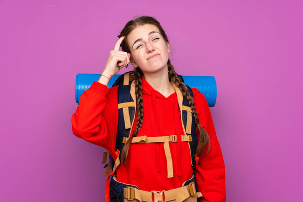 Jeune fille alpiniste avec un grand sac à dos sur fond violet isolé ayant des doutes et avec une expression du visage confus - Photo, image