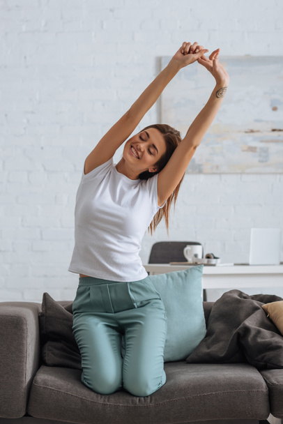 smiling woman stretching while chilling on sofa in living room  - Photo, Image