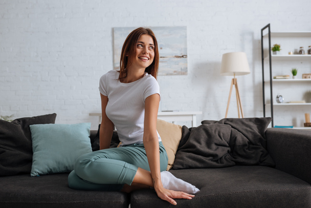 young smiling woman looking away while chilling on sofa in living room  - Photo, Image