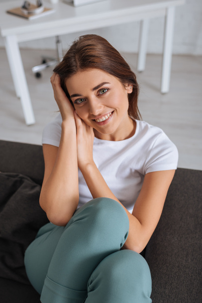 yleisnäkymä nuori hymyilevä nainen katselee kameraa rentoutuen olohuoneessa
  - Valokuva, kuva