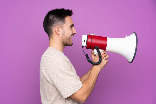 Young handsome man over isolated purple background shouting through a megaphone - Фото, зображення