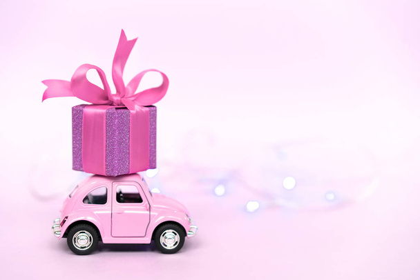 Voiture de jouet rétro rose livrant boîte cadeau pour la Saint-Valentin sur fond rose
. - Photo, image