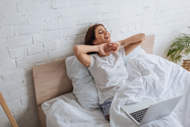 mujer soñadora sonriendo mientras se enfría en la cama cerca de la computadora portátil
   - Foto, imagen
