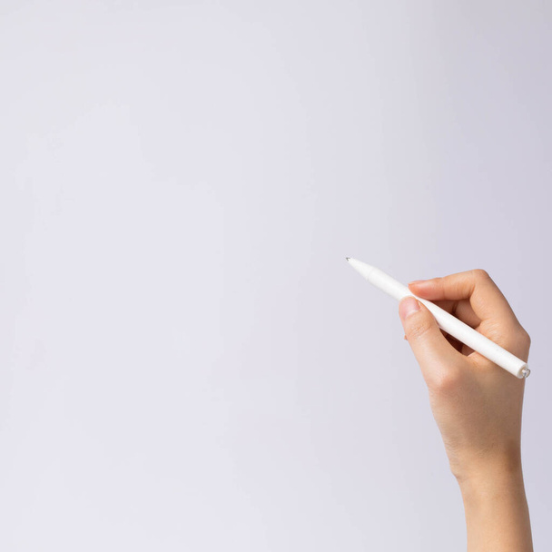 Nahaufnahme einer Hand, die einen weißen Stift auf weißem Hintergrund hält - Foto, Bild