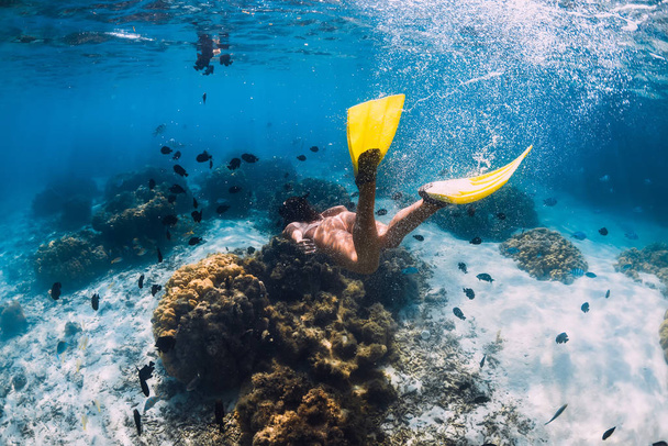 Freediver meisje met vinnen glijdt over zandige bodem in blauwe oceaan - Foto, afbeelding