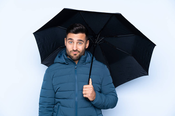 Mann hält Regenschirm mit traurigem Gesichtsausdruck über isoliertem Hintergrund - Foto, Bild