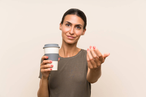 Young woman holding a take away coffee inviting to come with hand. Happy that you came - Photo, Image