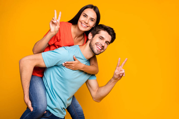 Profile photo of guy carrying lady piggyback summer adventures together showing v-sign symbols wear casual stylish blue orange t-shirts jeans isolated yellow color background - 写真・画像