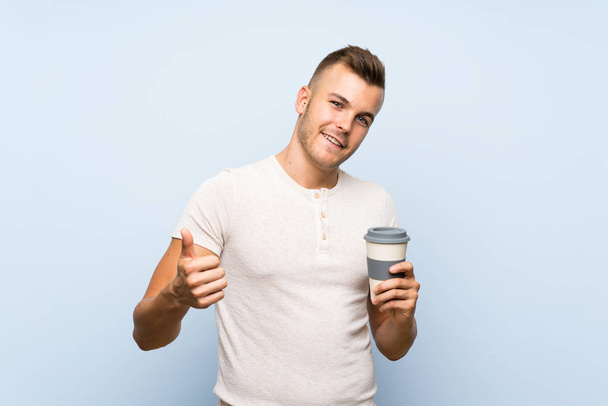 Joven guapo hombre rubio sobre aislado fondo azul sosteniendo taza caliente de café
 - Foto, Imagen